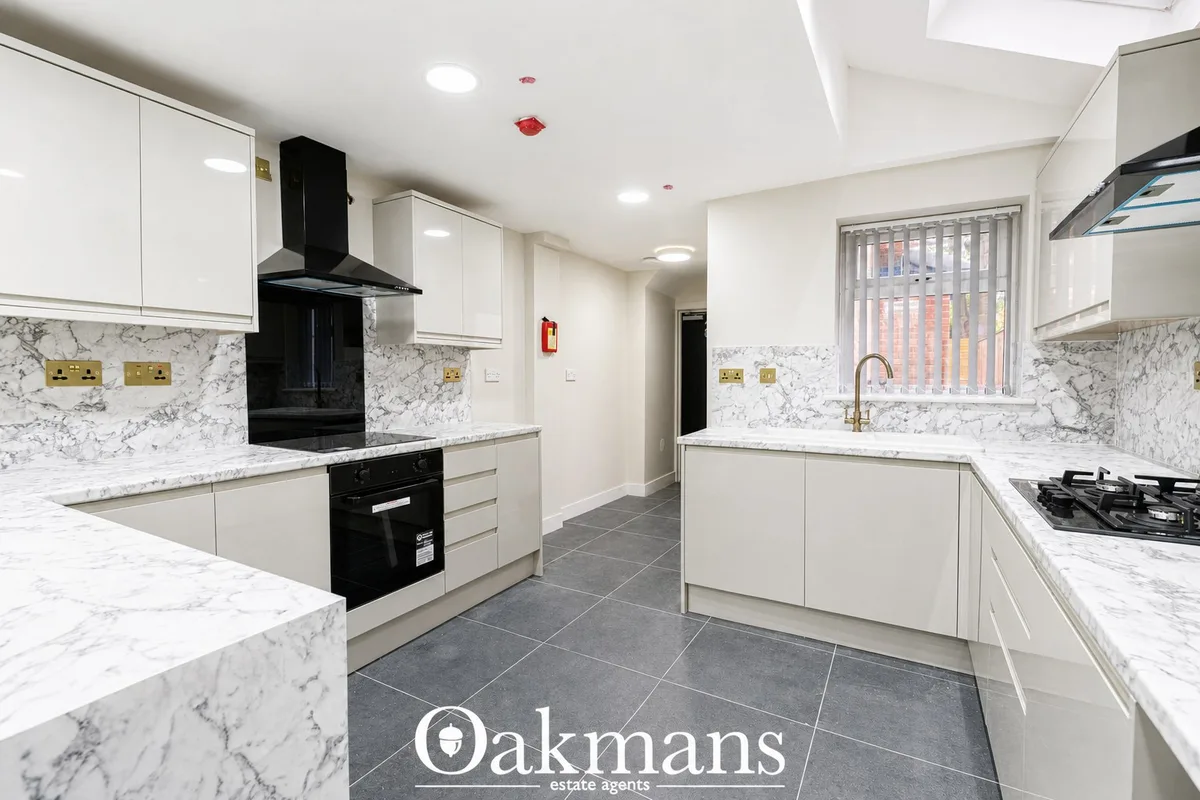 Modern fitted kitchen with white units, marble worktops, black built-in oven and hob, island with breakfast bar, and gre