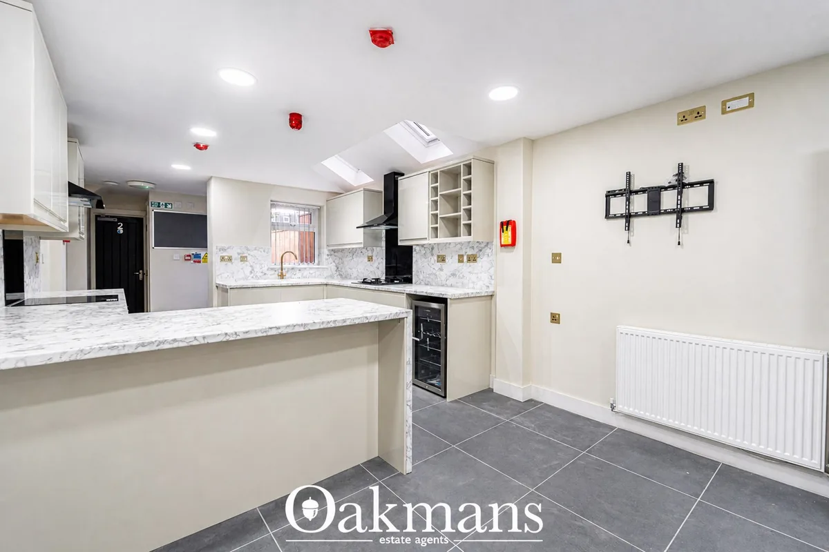 Modern fitted kitchen with white units, marble worktops, black built-in oven, breakfast bar island, skylights and dark t