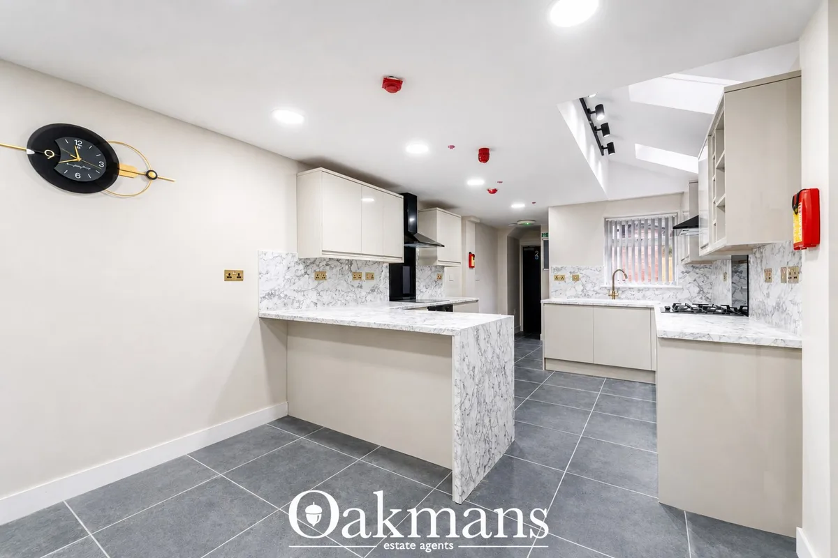 Modern fitted kitchen with white units, marble worktops, breakfast bar island, dark tile flooring, gas hob and recessed 