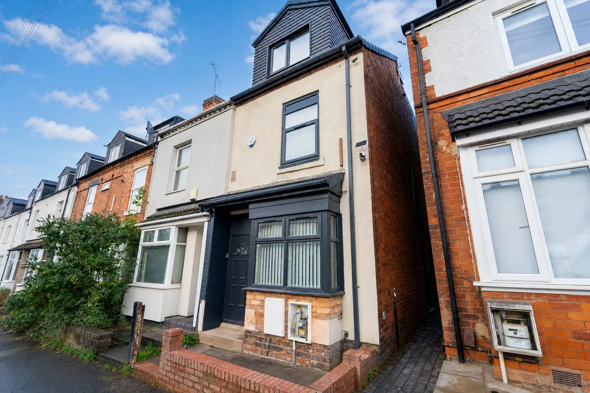 Cream and black terraced house with mansard roof, dark blue entrance door, brick chimneys, and neighbouring red brick pr