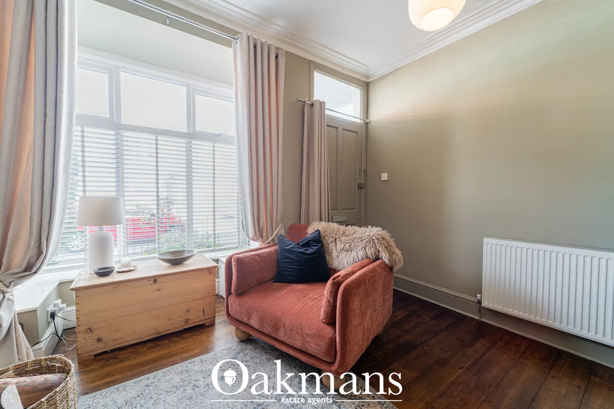 Bright living room with terracotta armchair, large bay window with shutters and pink curtains, wooden storage chest, dar