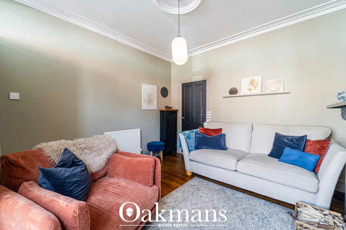 Light living room with cream walls, two sofas in white and coral, blue and red scatter cushions, wooden flooring, pendan