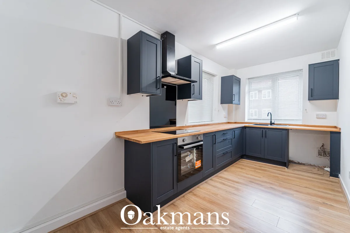 Modern fitted kitchen with dark blue cabinetry, wooden worktops, integrated oven, and induction hob. White walls and cei