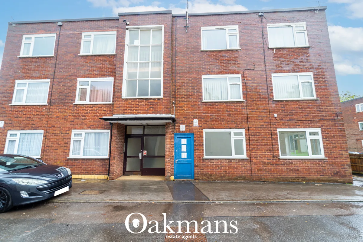 Red brick apartment building with white framed windows, blue entrance door, and parked car in front on residential stree