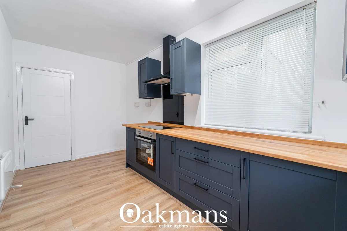 Modern kitchen with dark blue fitted units, wooden worktops, built-in oven and hob, white blinds on window, wooden floor