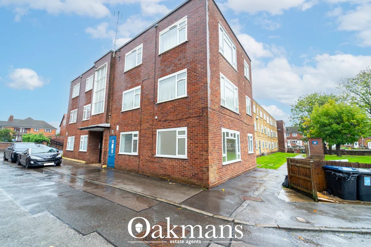 Red brick corner apartment building with white window frames, blue entrance door, wet paved forecourt and parked car