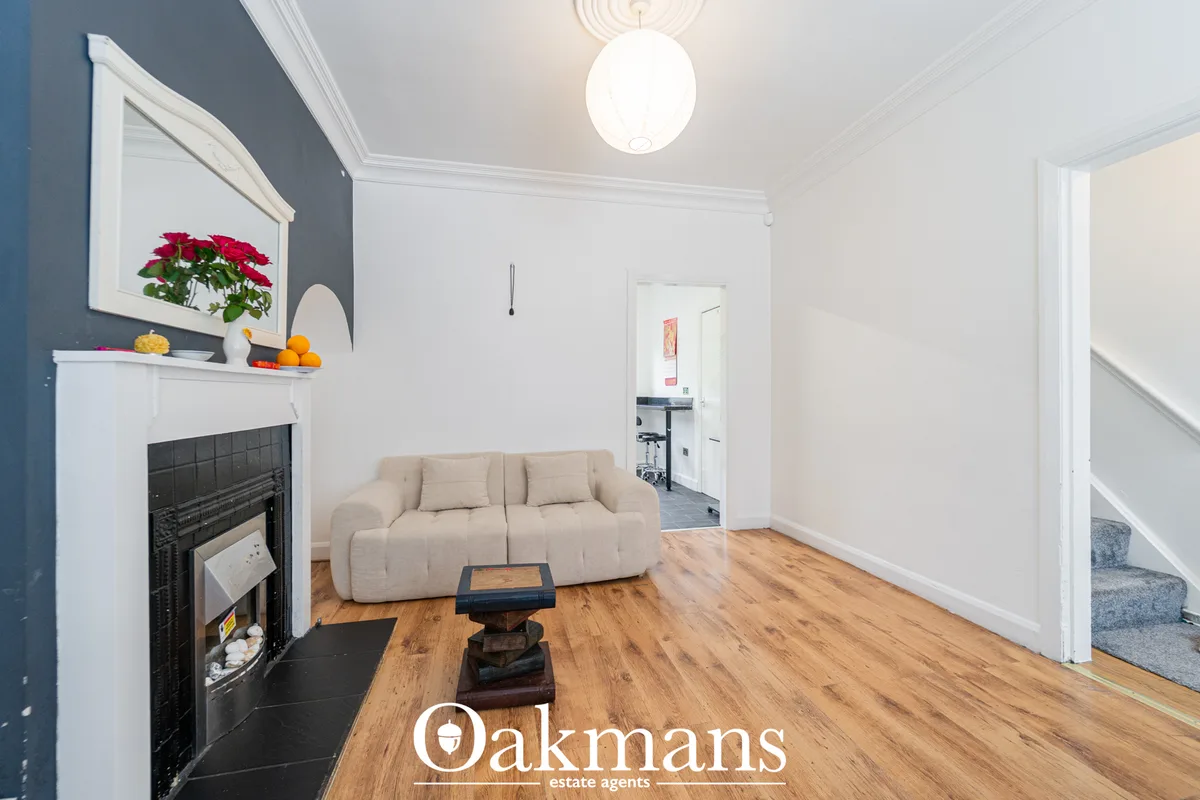 Bright living room with cream sofa, fireplace with decorative mantelpiece, wooden flooring, white walls and pendant ligh