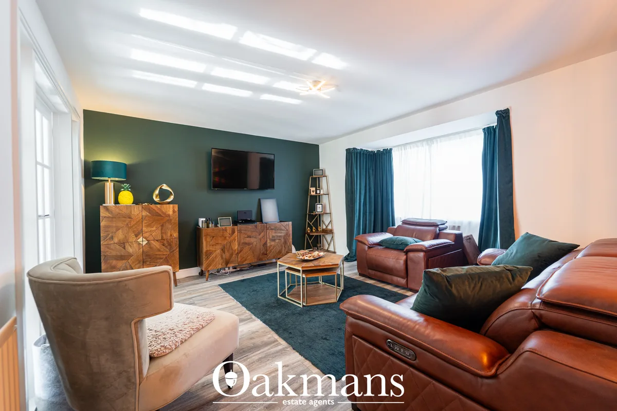 Modern living room with cognac leather seating, dark teal accent wall, wooden storage units, wall-mounted TV, and large 