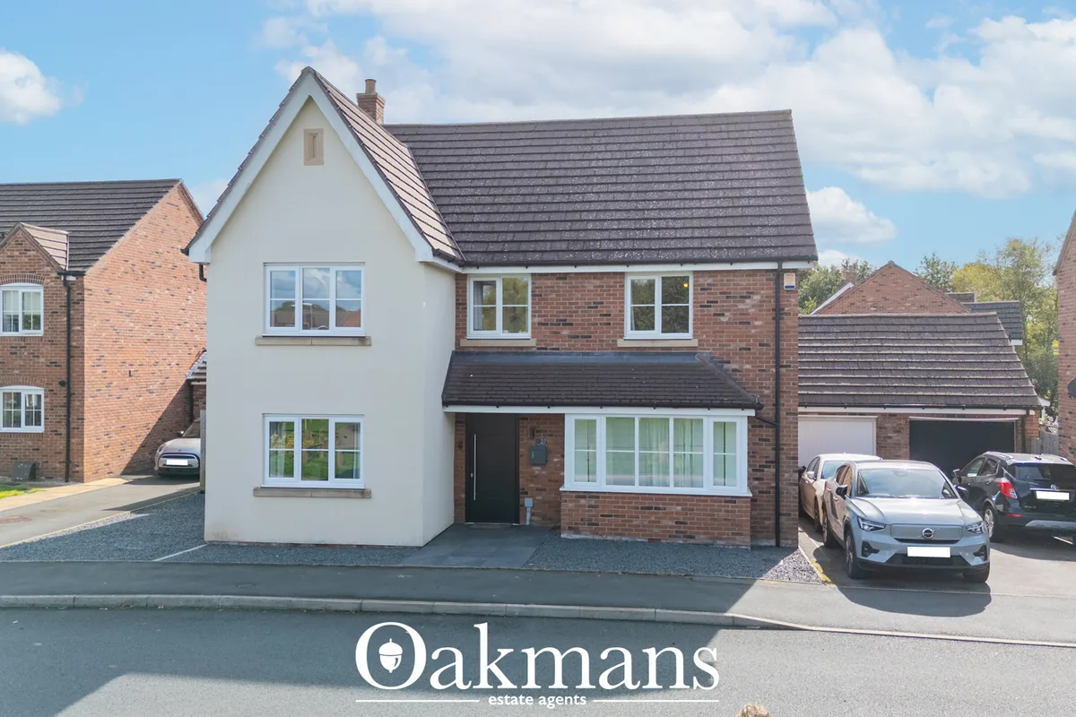 Modern two-storey brick and rendered house with dark roof tiles, driveway, garage, and parked cars in suburban street
