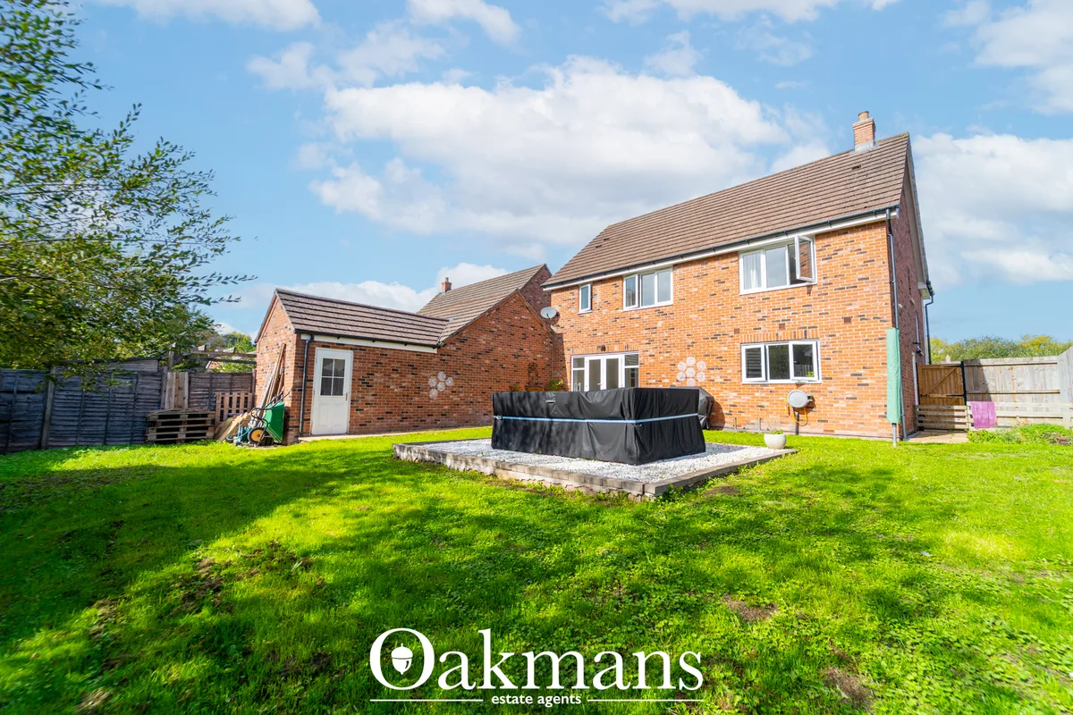 Rear garden with lawn, trampoline, brick two-storey house, wooden fencing and clear sky