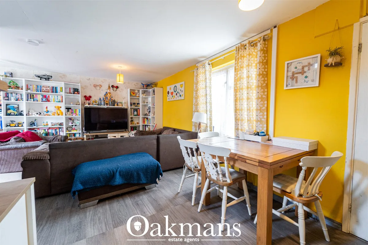 Bright yellow living room with dark grey sofa, wooden dining table with white chairs, built-in shelving, TV, and yellow-
