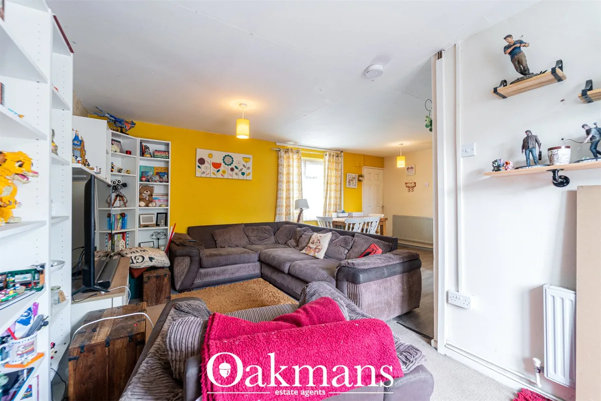 Bright living room with vibrant yellow accent wall, grey corner sofa, wooden shelving, white storage units and yellow pe