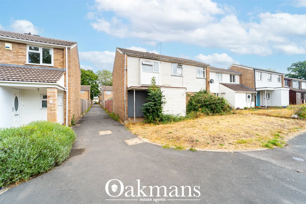 Row of suburban semi-detached houses with brick and rendered frontages, driveways and overgrown forecourt under clear bl