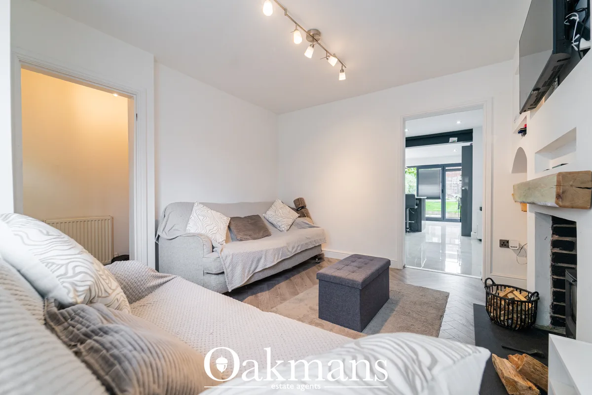 Bright living room with two sofas, dark ottoman, track lighting, French doors to garden, fireplace with wooden mantel an