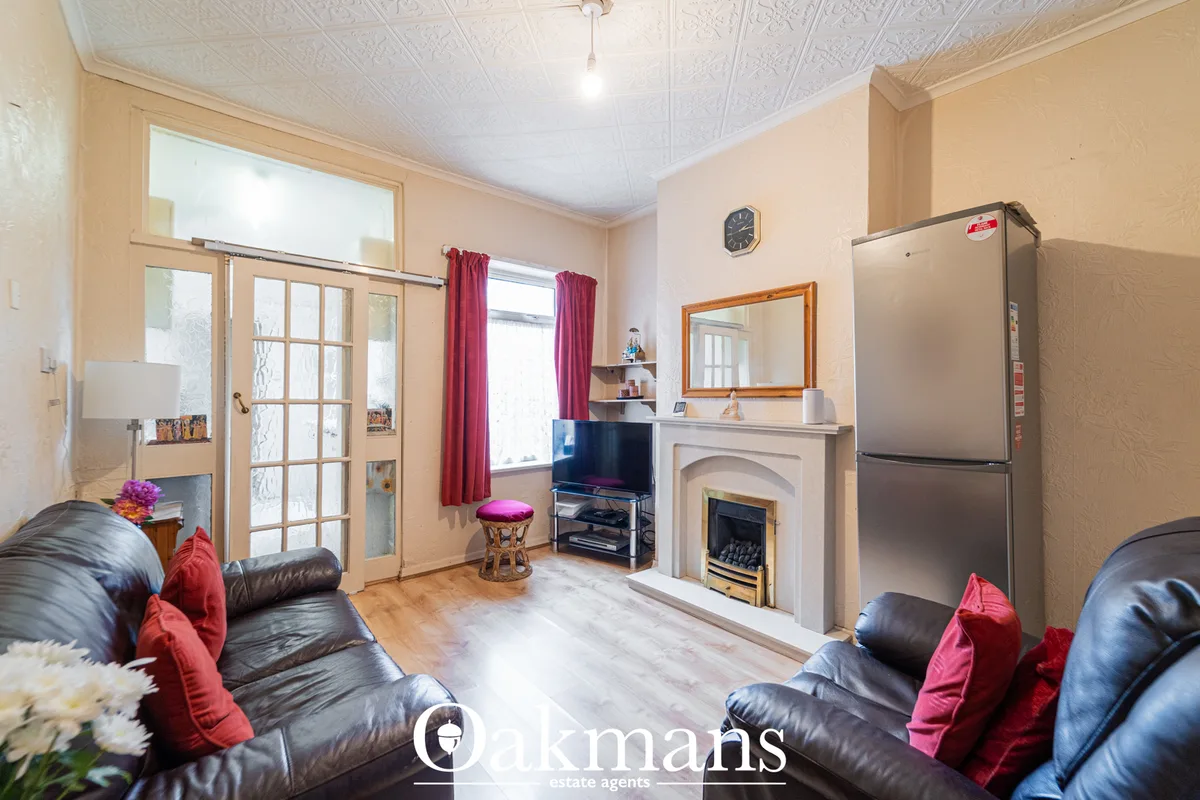 Spacious living room with black leather sofas, decorative cushions, fireplace with mirror, TV on stand, and access to ga