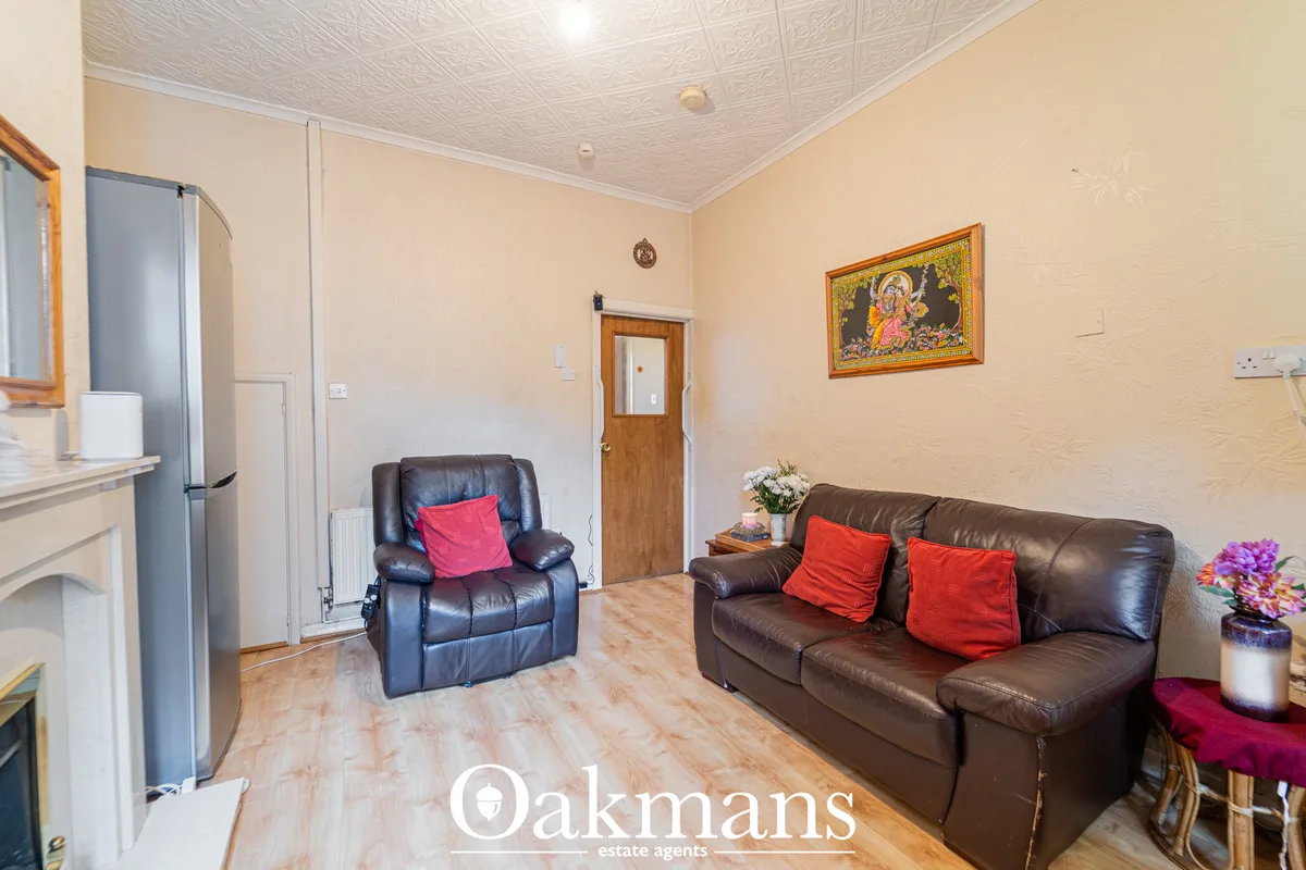 Living room with brown leather sofa and recliner chair, red cushions, cream walls, wooden door, decorative artwork and p