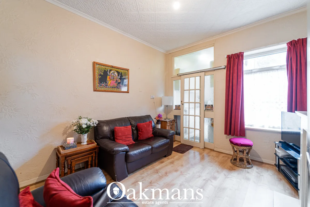Spacious living room with dark leather sofa, red cushions, wooden side table, ornamental religious artwork, French doors