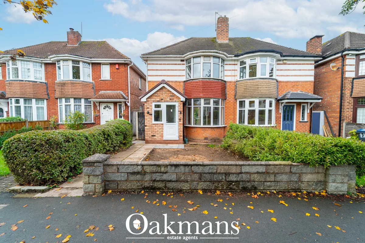 Brick semi-detached house with bay windows, white entrance door, hedge frontage and stone boundary wall