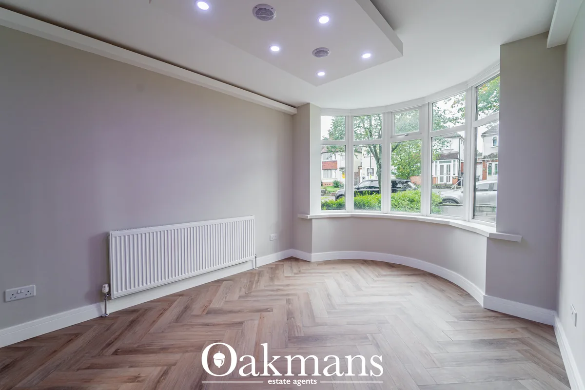 Bright living room with bay window, herringbone wood flooring, pale lilac walls, white radiator and recessed ceiling lig