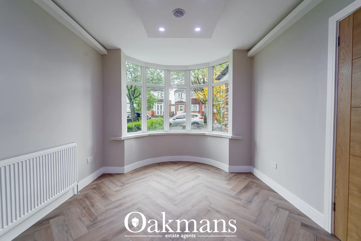 Bright living room with curved bay window, herringbone wood flooring, white ceiling with recessed lighting, radiator and
