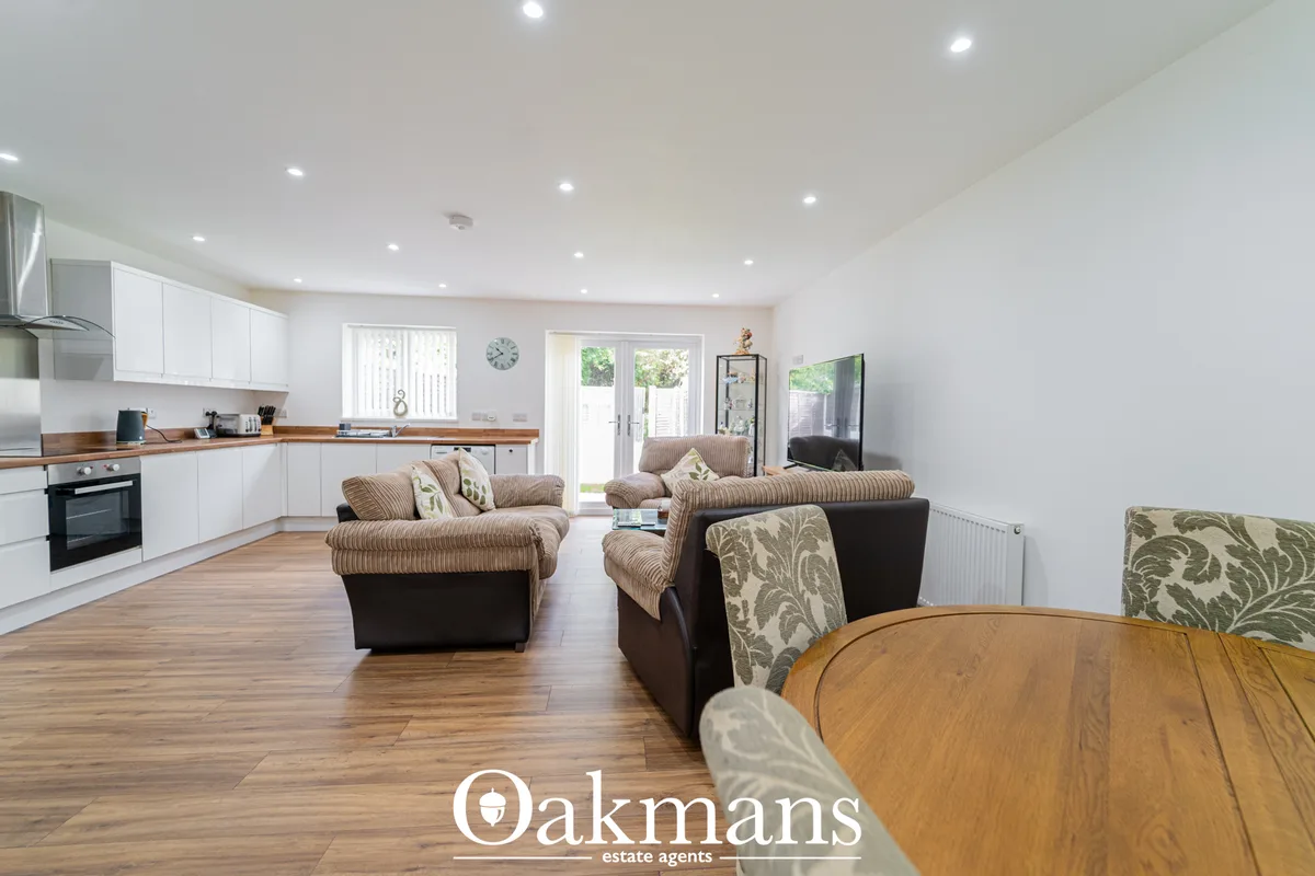 Open-plan living room with brown upholstered armchairs, wooden dining table, white fitted kitchen with wood worktops, gl