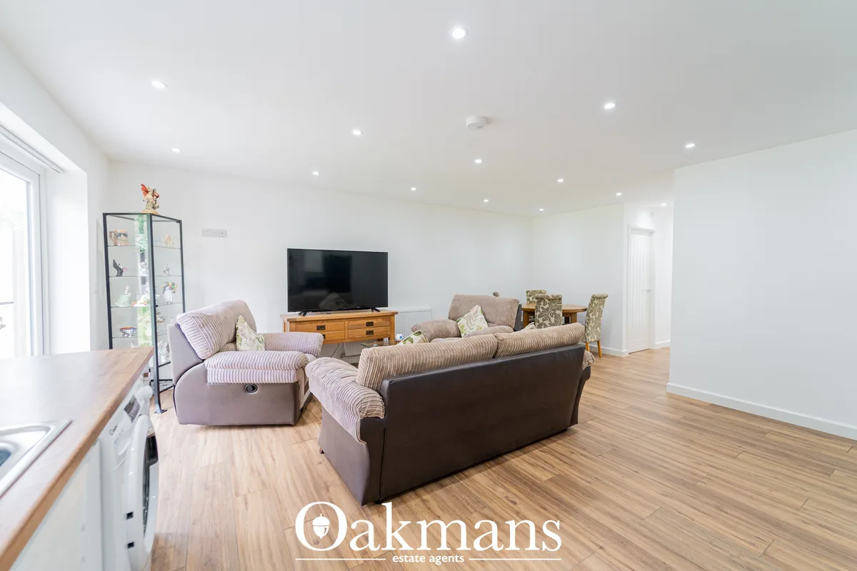 Spacious living room with two fabric sofas, wooden TV unit, recessed ceiling lights, wooden flooring, and patio doors to