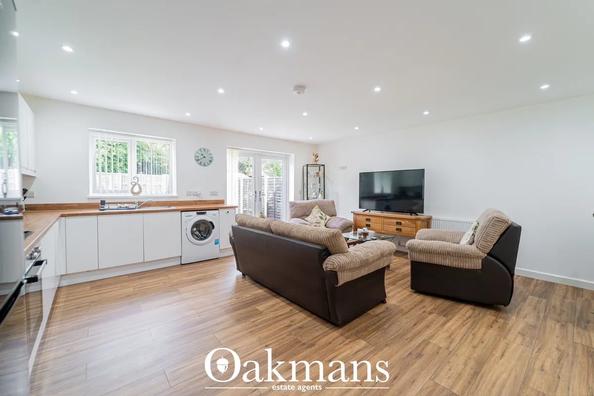 Open-plan living room with cream and brown upholstered sofa, wooden TV unit, wall-mounted flat-screen TV, recessed ceili