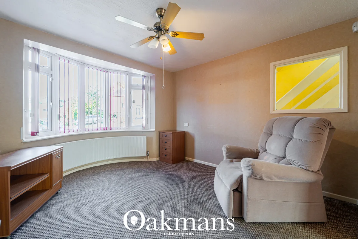 Spacious living room with beige walls, cream recliner chair, wooden furniture, large bay window with vertical blinds, ce