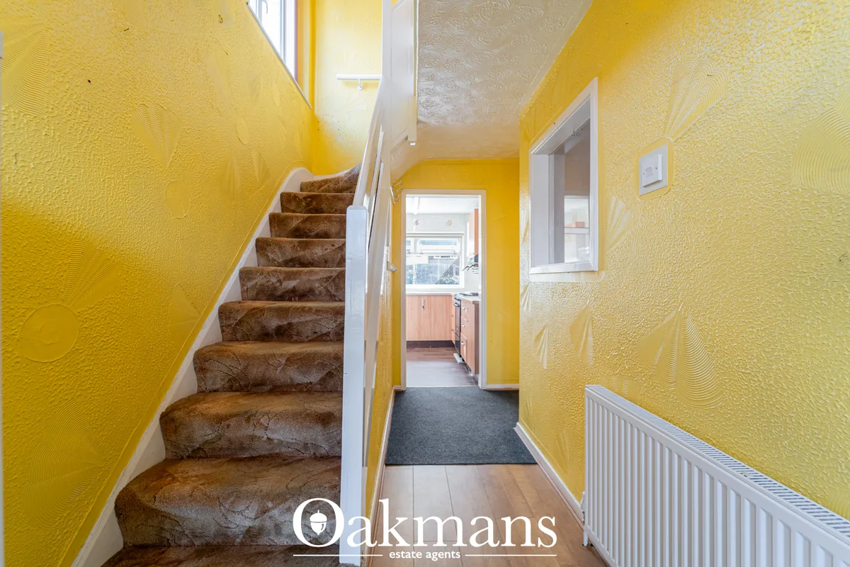 Bright yellow textured hallway with brown carpet staircase, white radiator, doorway to kitchen visible ahead
