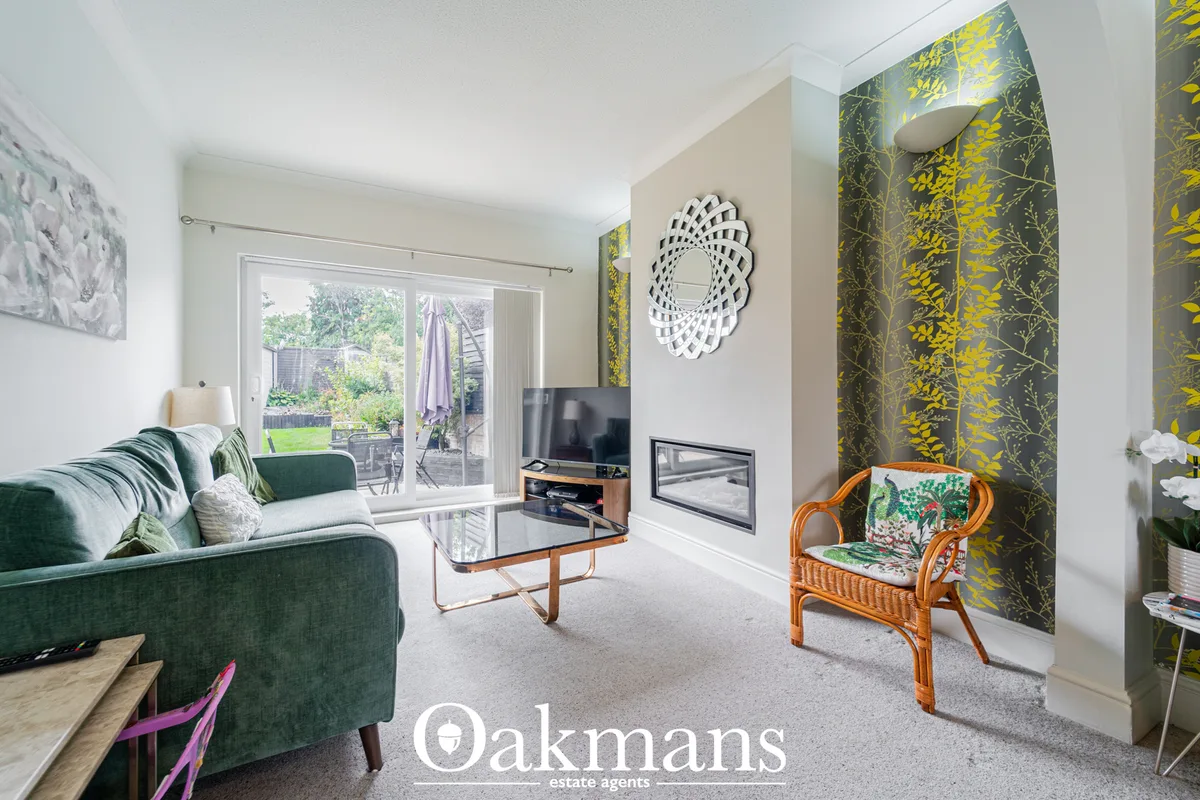 Bright living room with green upholstered sofa, fireplace, TV unit, patterned wallpaper accent wall, wicker chair, and g