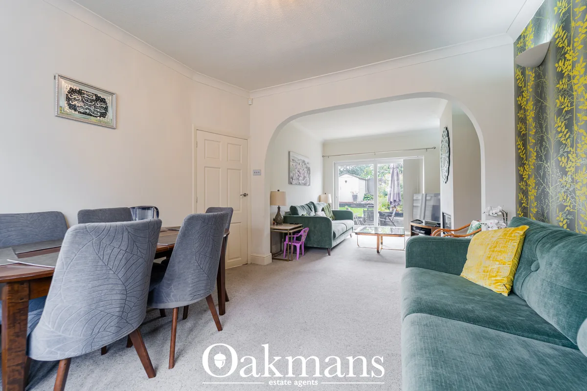 Bright open-plan living space with green upholstered sofa, dining chairs, archway to garden room, yellow patterned curta