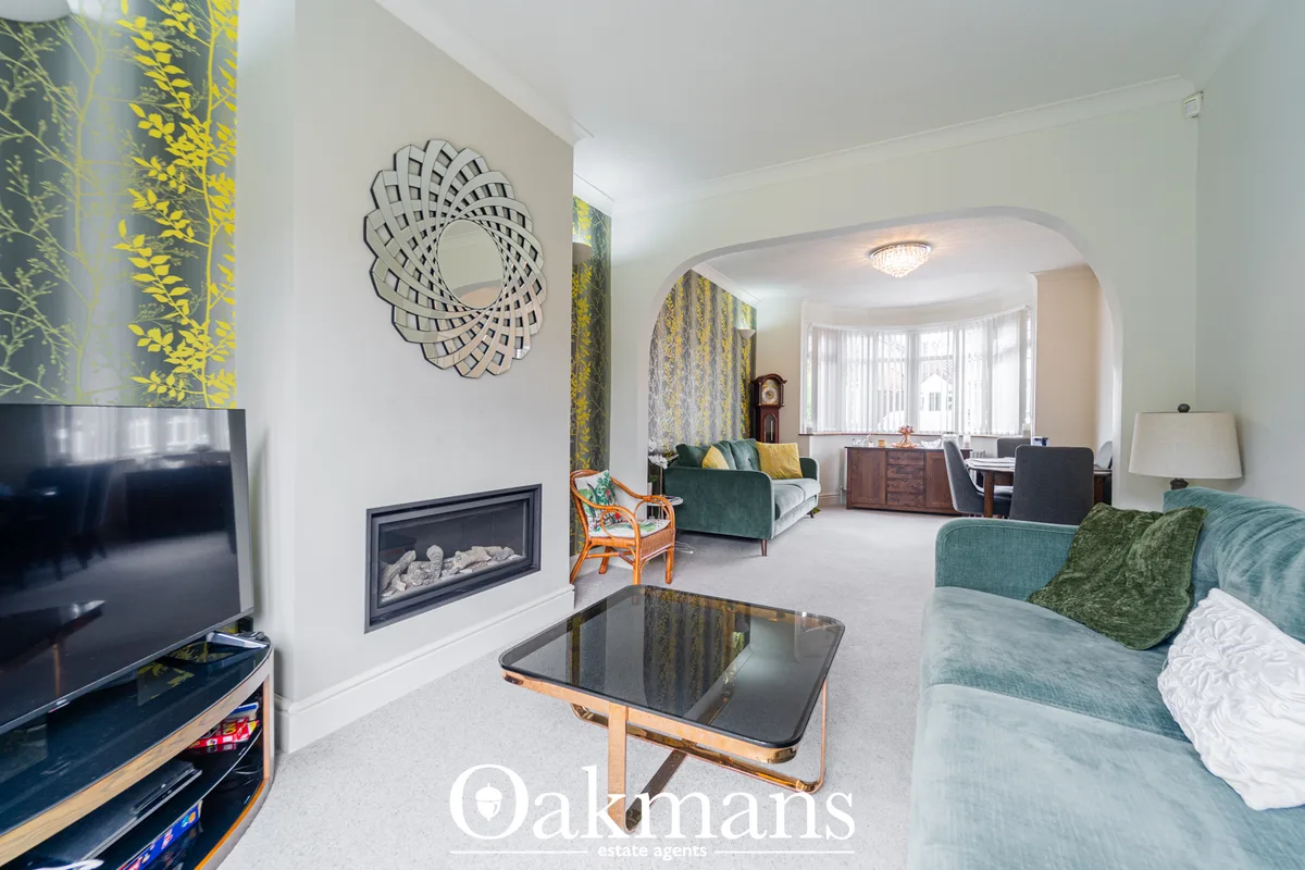 Spacious living room with teal sofa, fireplace, decorative mirror, TV, and bay window overlooking gardens