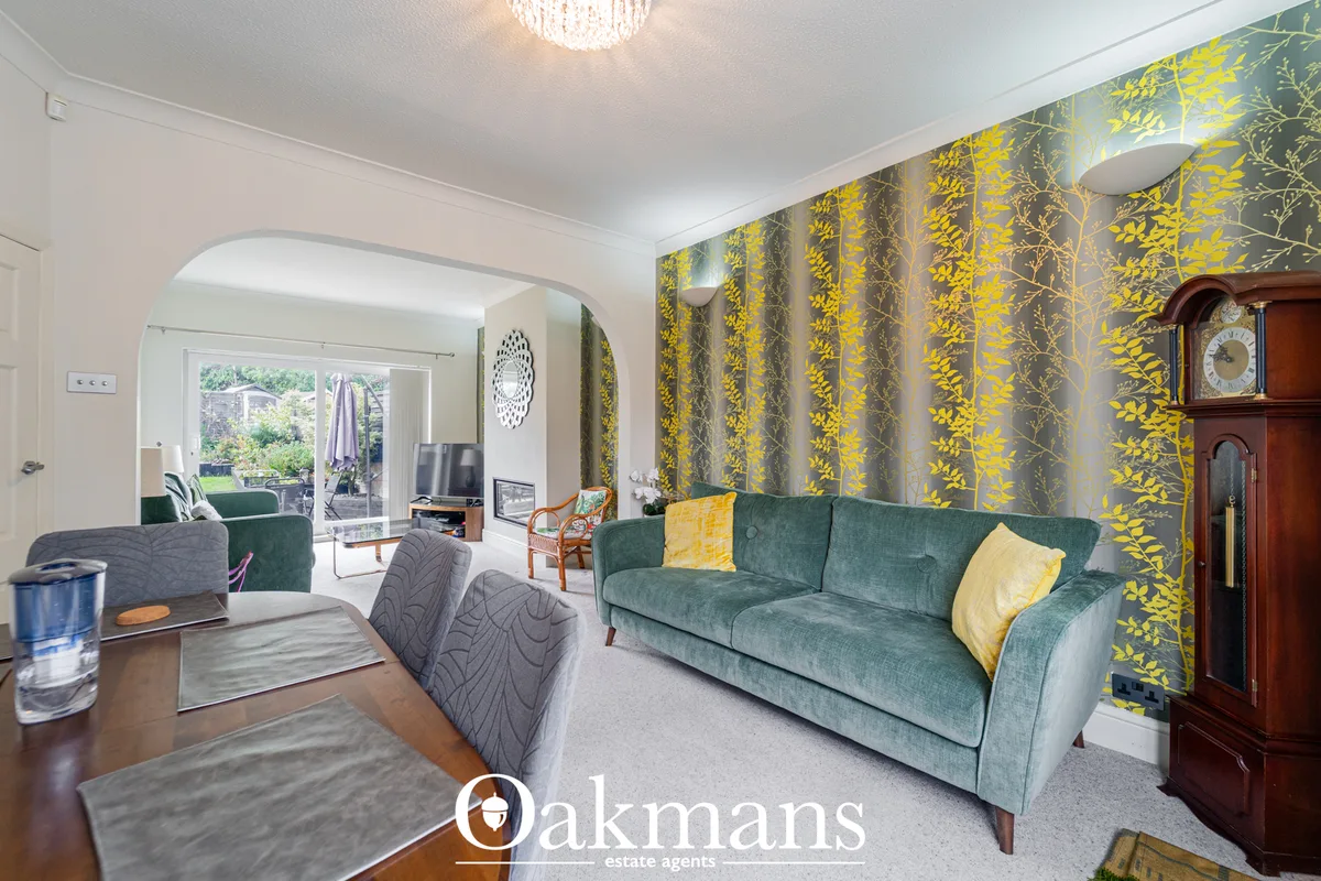 Spacious living room with green velvet sofa, yellow leaf-patterned wallpaper, wooden furniture, crystal chandelier and g