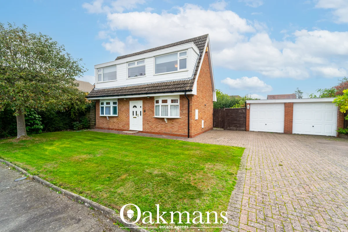Brick-built detached house with white UPVC windows, pitched roof, drive and dual garages. Well-maintained front garden w