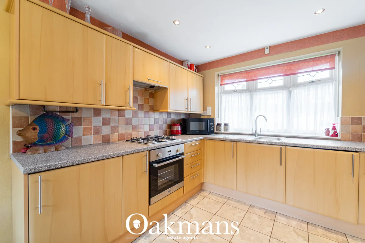 L-shaped fitted kitchen with honey oak cabinets, granite worktops, tiled backsplash, gas hob, built-in oven, and window 