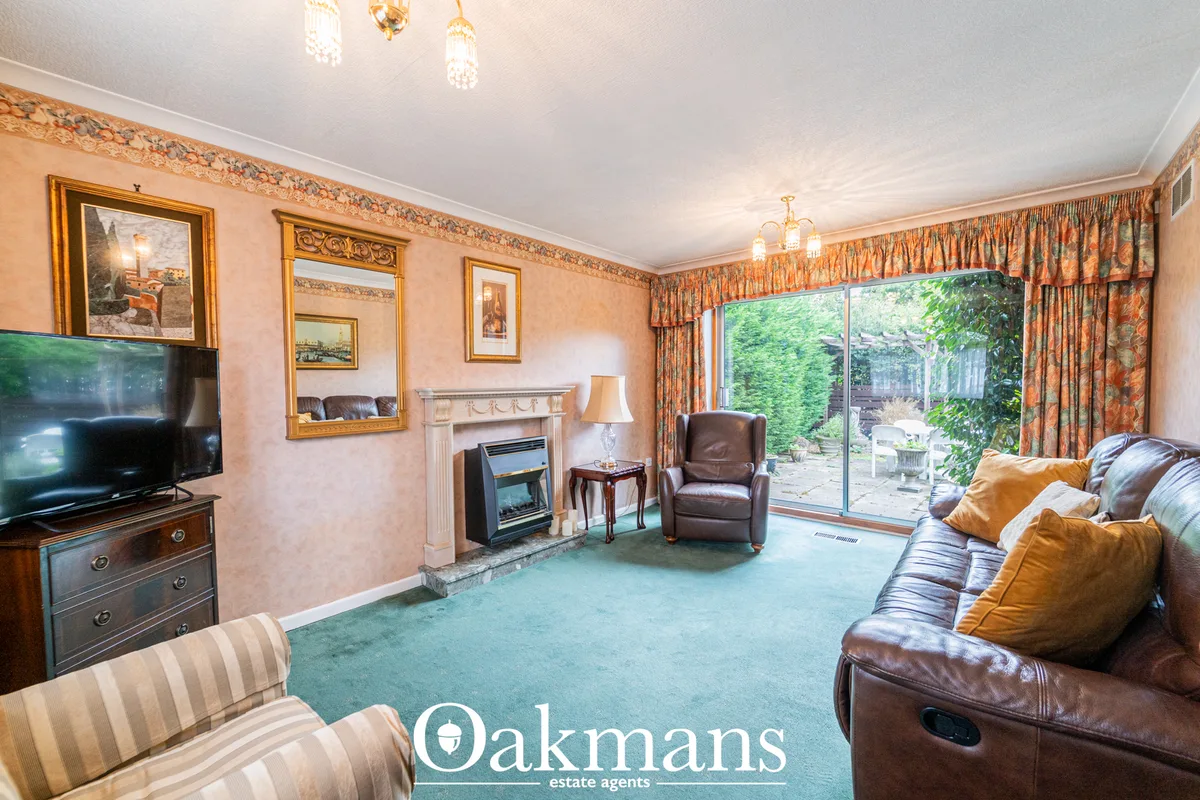 Spacious living room with brown leather sofa, fireplace, patio doors to garden, peach wallpaper, gold framed mirrors and