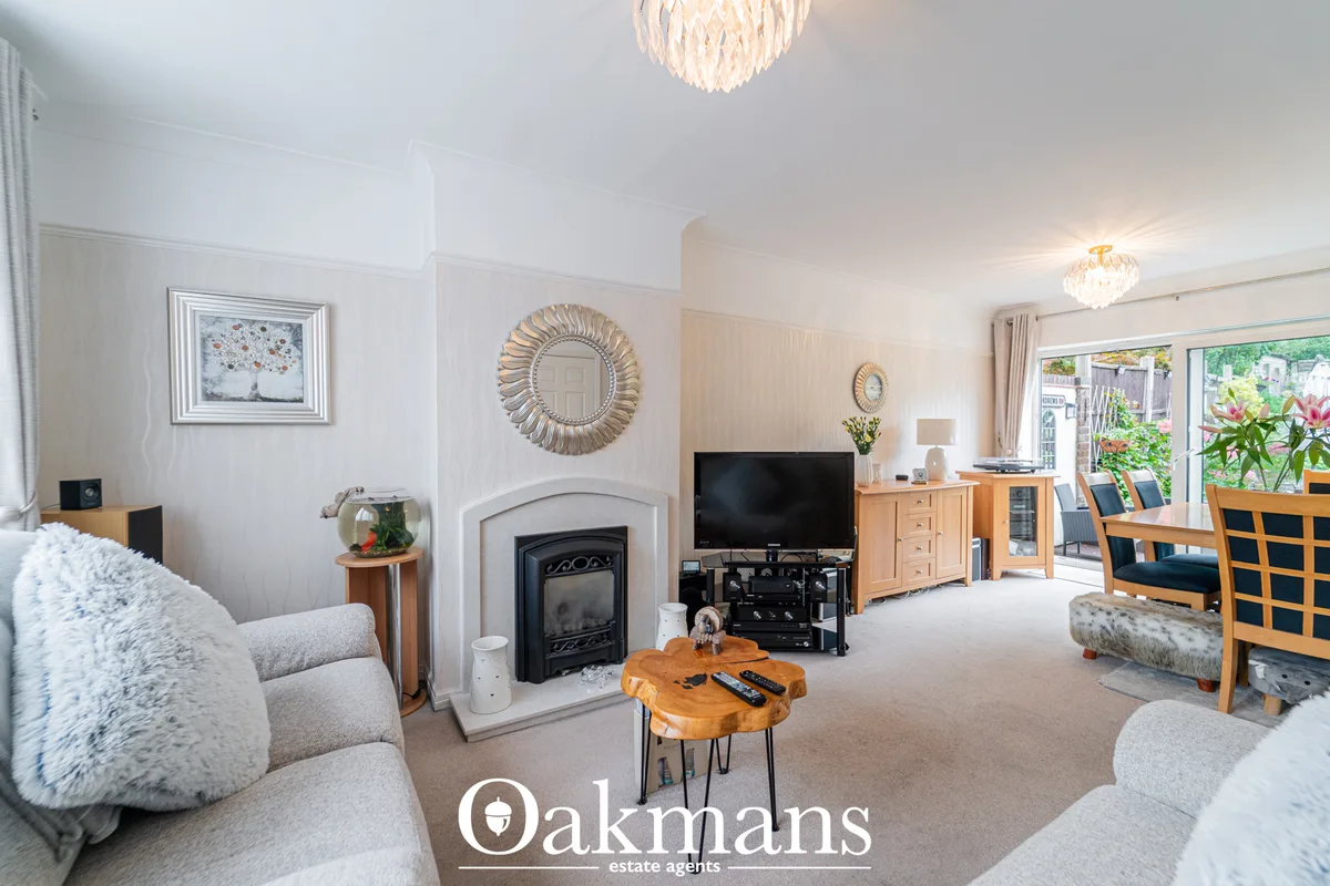 Spacious living room with cream carpet, white walls, fireplace with black stove insert, flat-screen TV, wooden furniture