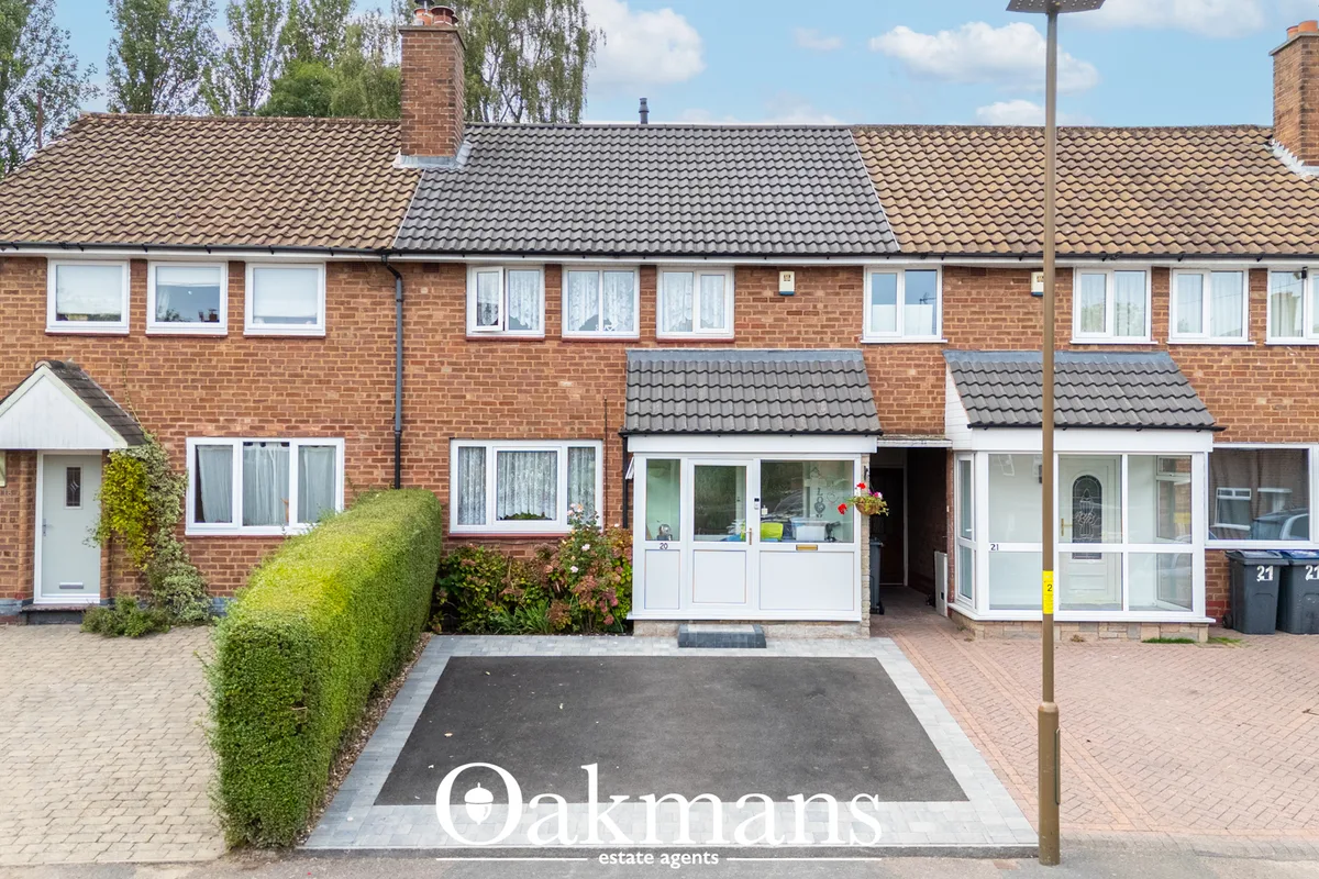 Red brick terraced house with tiled roof, white-framed windows and conservatory porches, brick driveway and mature hedgi