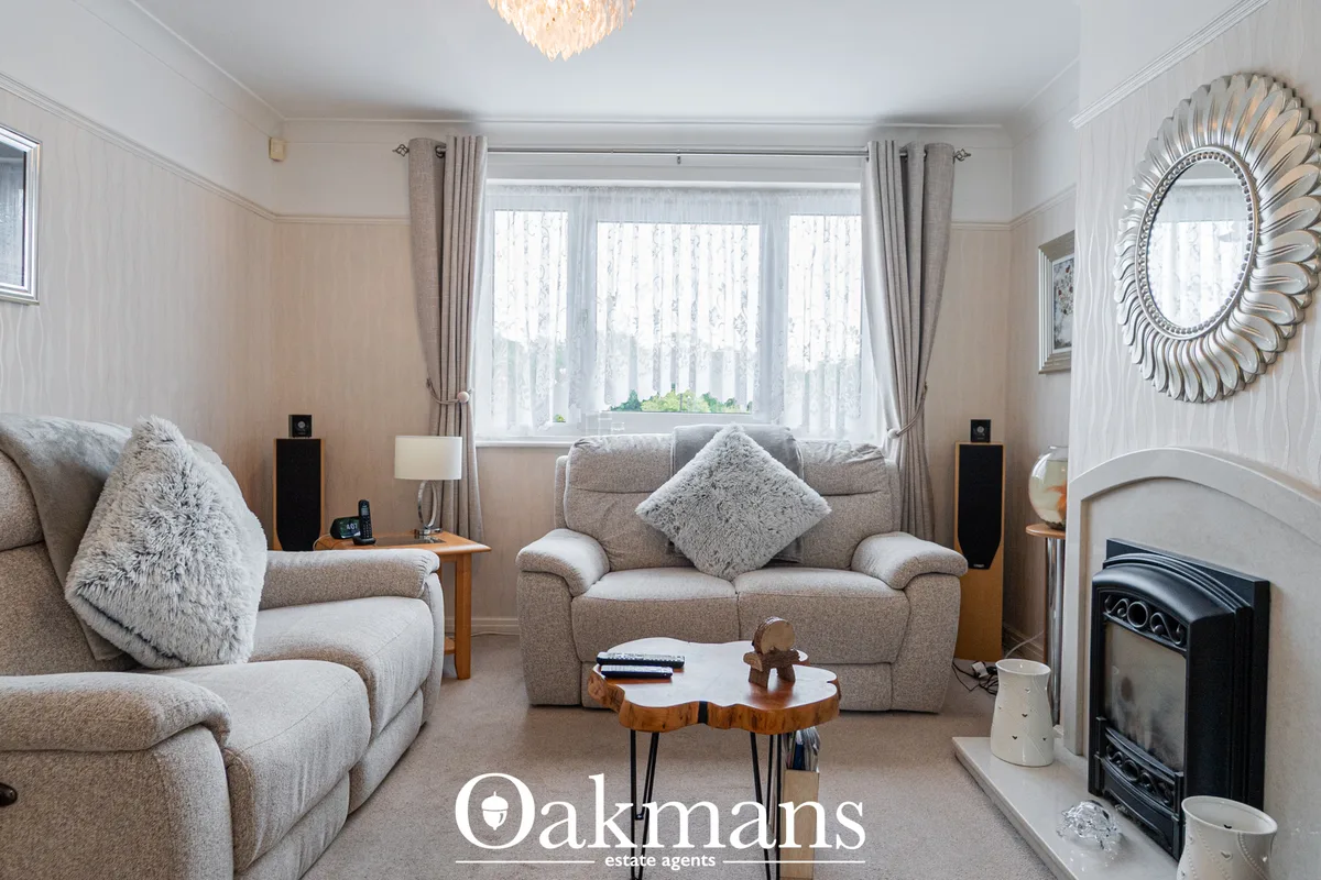 Bright living room with two beige sofas, fireplace, decorative mirror, large windows with sheer curtains and view of tre