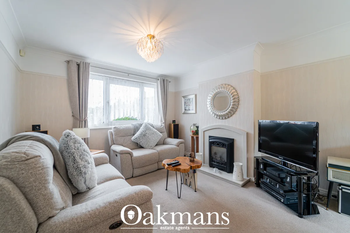 Spacious living room with beige upholstered furniture, fireplace with decorative surround, TV on stand, ornamental mirro