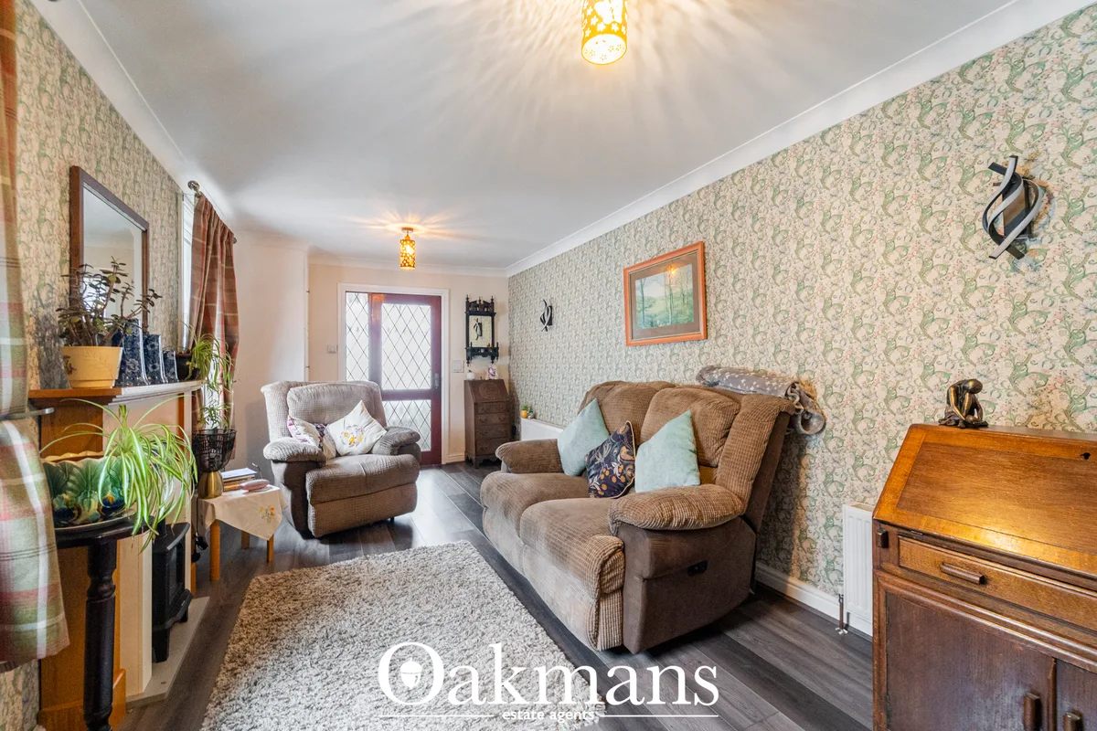 Living room with patterned wallpaper, two upholstered armchairs and sofa with scatter cushions, wooden furniture, potted