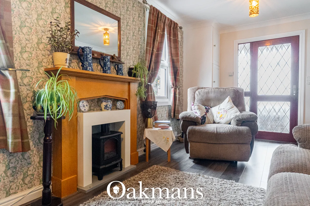 Living room with patterned wallpaper, feature fireplace with wooden surround, upholstered armchair, glazed door to garde
