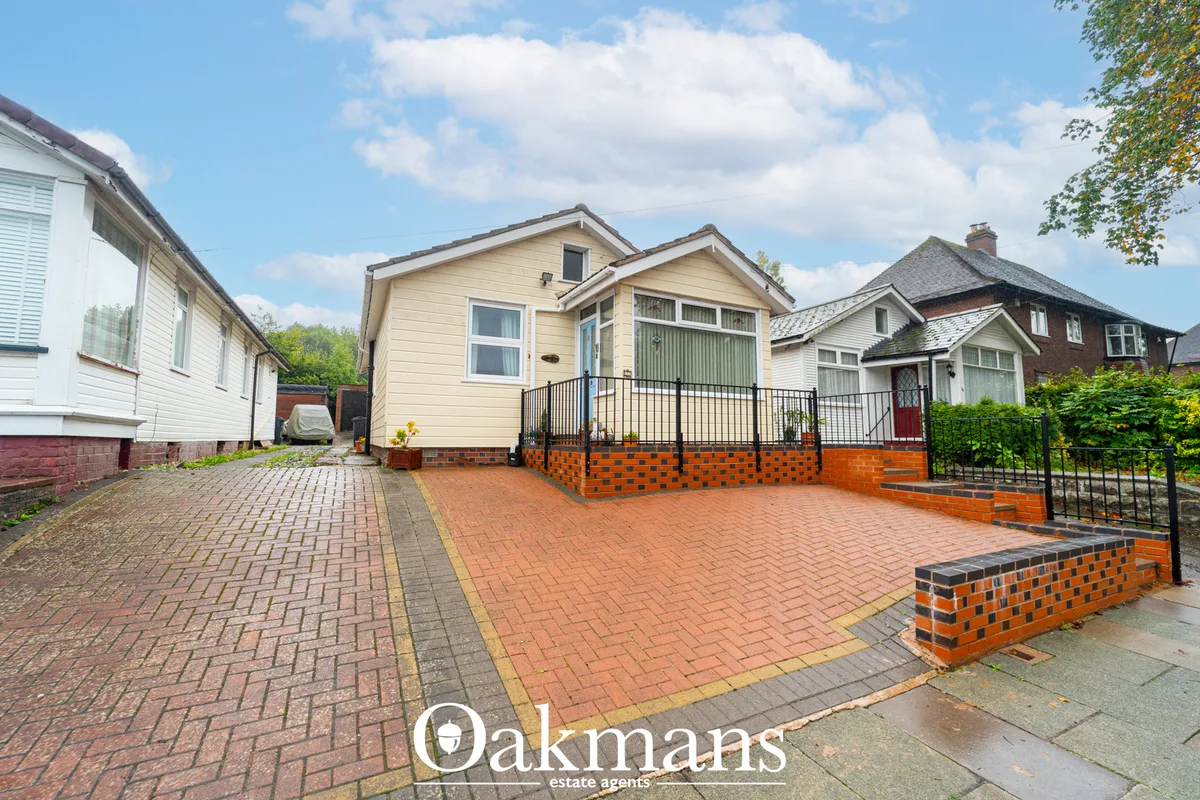 Brick and cream rendered bungalow with black railings, brick driveway, black metal gates and green hedging to sides