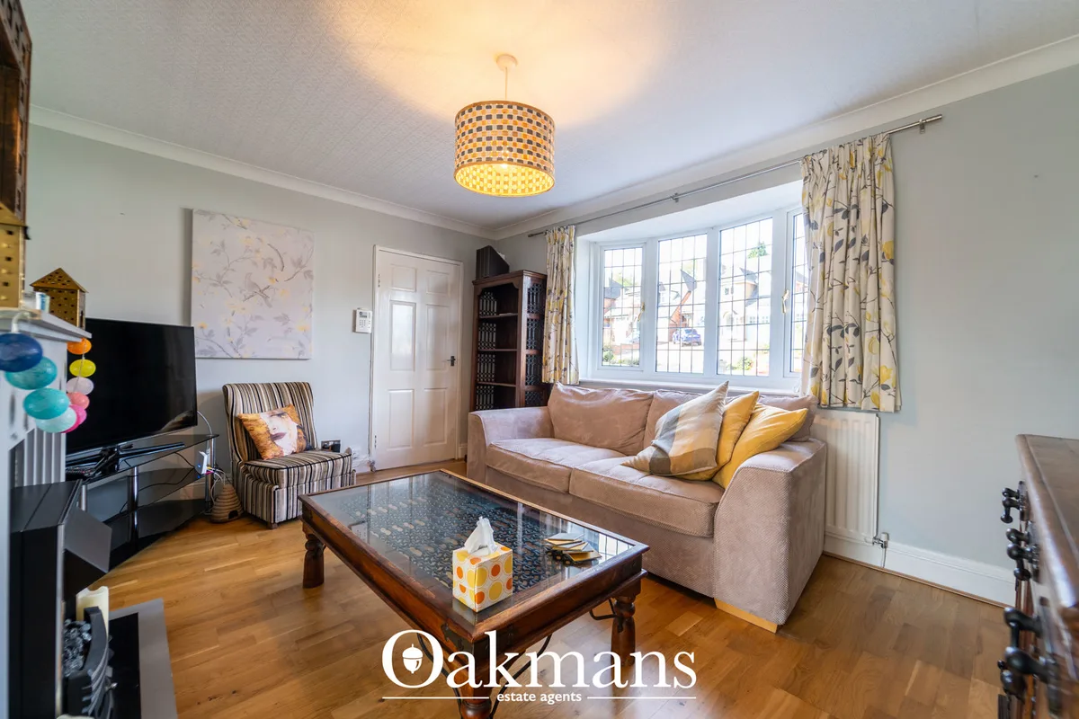 Bright living room with beige sofa, wooden coffee table, striped armchair, large windows with patterned curtains, wooden