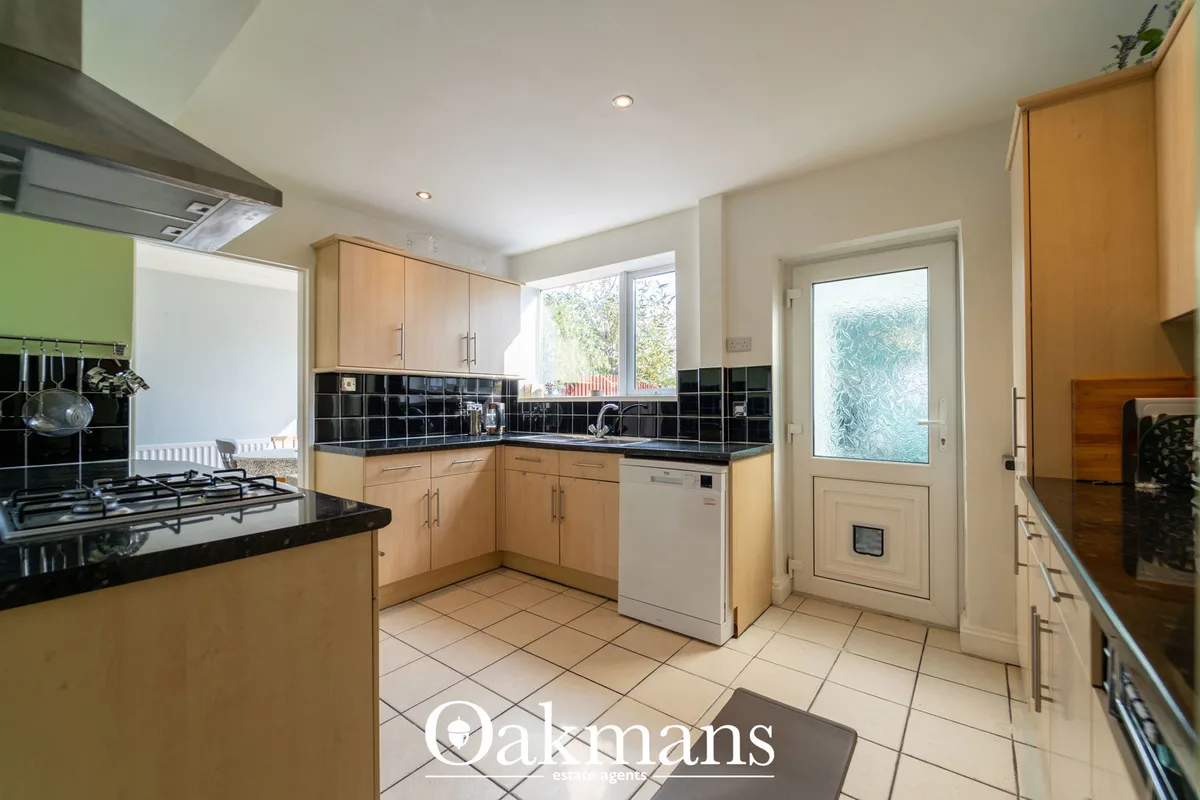 Modern fitted kitchen with light wood cabinetry, black granite worktops, gas hob, integrated dishwasher and black tile s