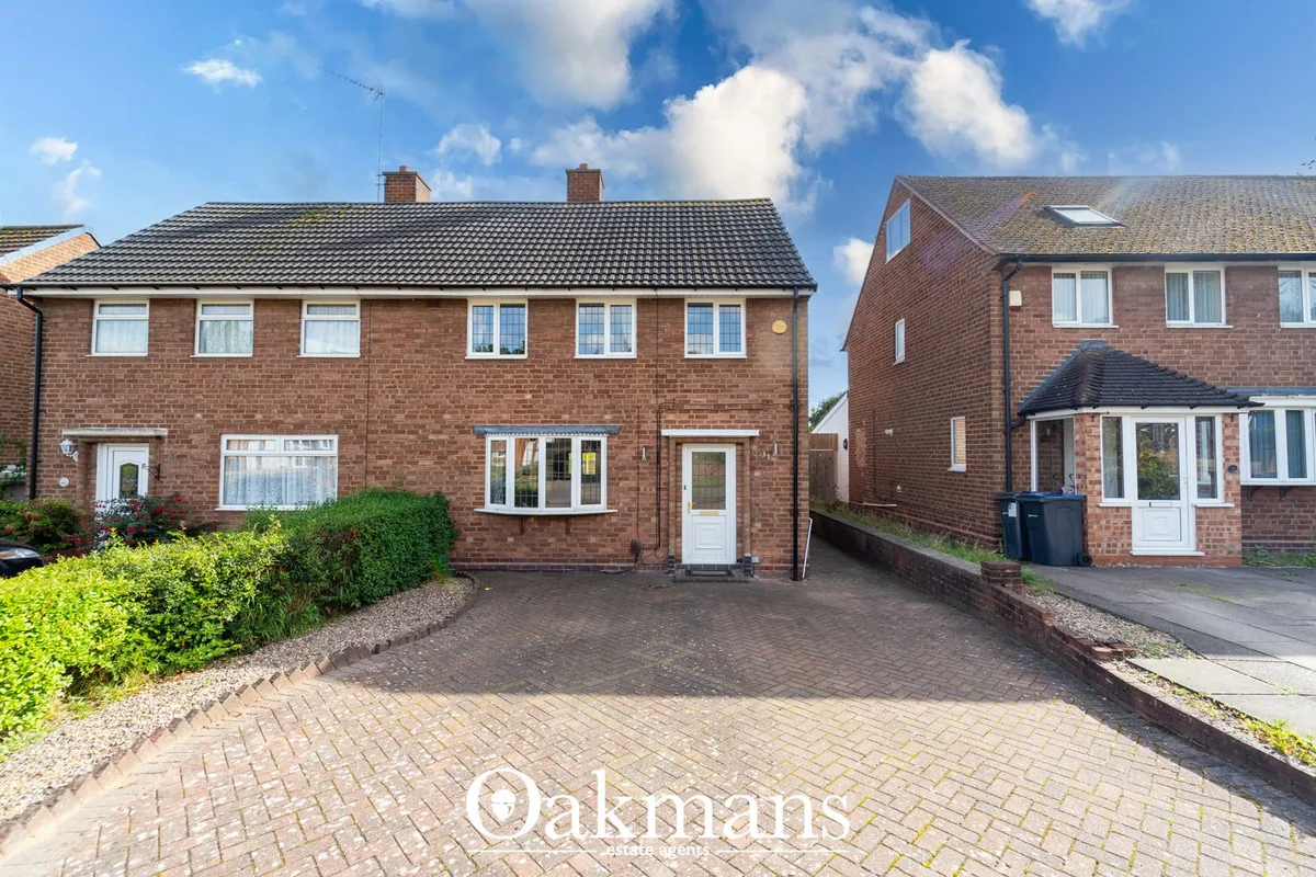 Semi-detached brick house with six windows, dark tiled roof, white-framed entrance door, brick driveway and low hedging