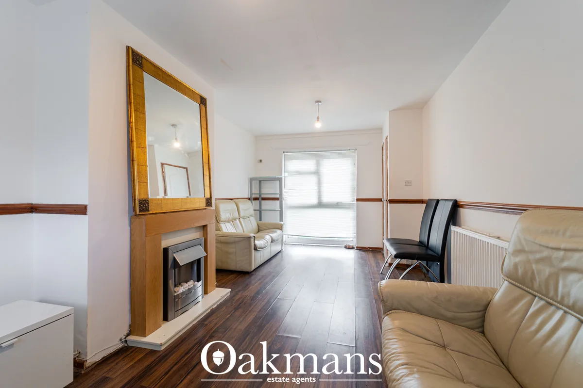 Spacious living room with wooden fireplace, large mirror, cream leather armchairs, dark wooden flooring, and patio doors