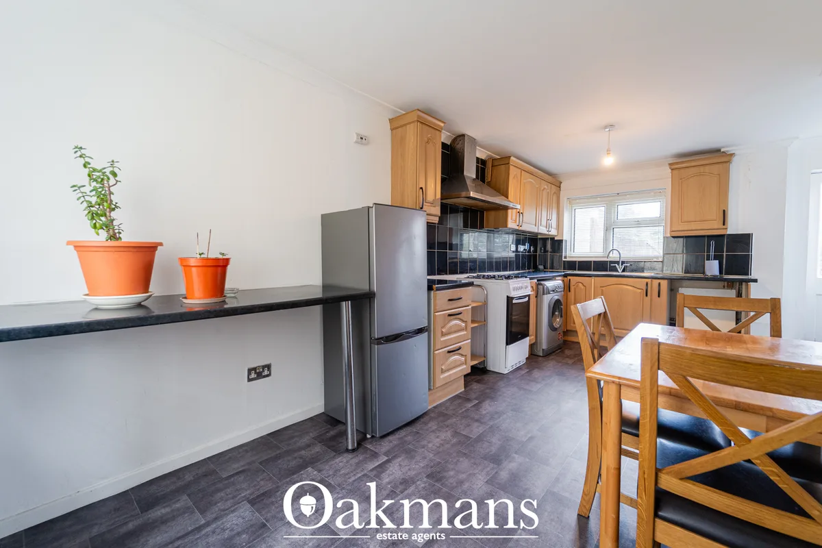 Open-plan kitchen with wooden cabinetry, stainless steel appliances, dark tile flooring, breakfast bar, dining table and