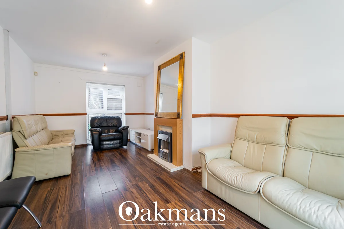 Spacious living room with cream leather sofas, dark wood flooring, fireplace with wooden surround and large mirror, wood