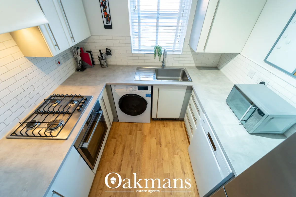 Modern fitted kitchen with white cabinetry, gas hob, integrated appliances, stainless steel sink and wooden flooring